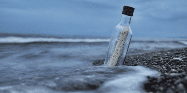 Een glazen fles met een oprolbriefje aangespoeld op een verlaten zandstrand