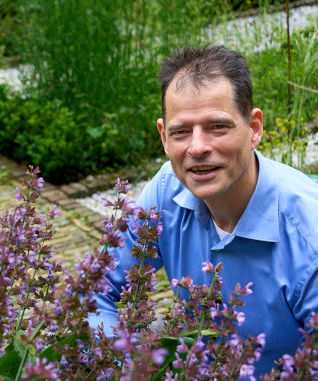 Iwan Koenderman in een blauw shirt in de Botanische Tuin bij het Universiteitsmuseum Utrecht, ruikend aan paarse bloemen